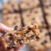 Hang holding an almond butter oatmeal cookie bar with more cookie bars in the background.