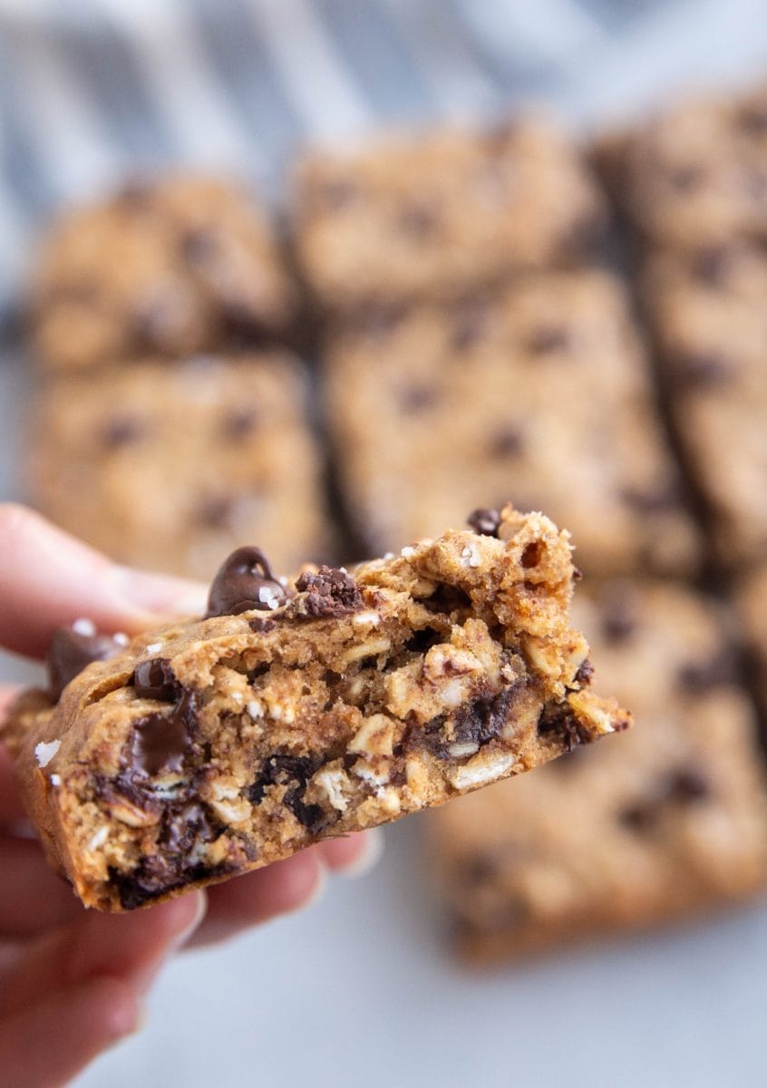 Hang holding an almond butter oatmeal cookie bar with more cookie bars in the background.