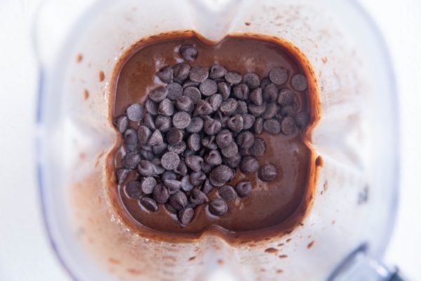 high-speed blender full of black bean brownie batter with chocolate chips ready to be mixed in.