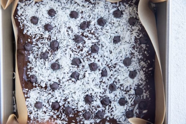 Square baking pan with brownie batter inside, sprinkled with coconut flakes and chocolate chips