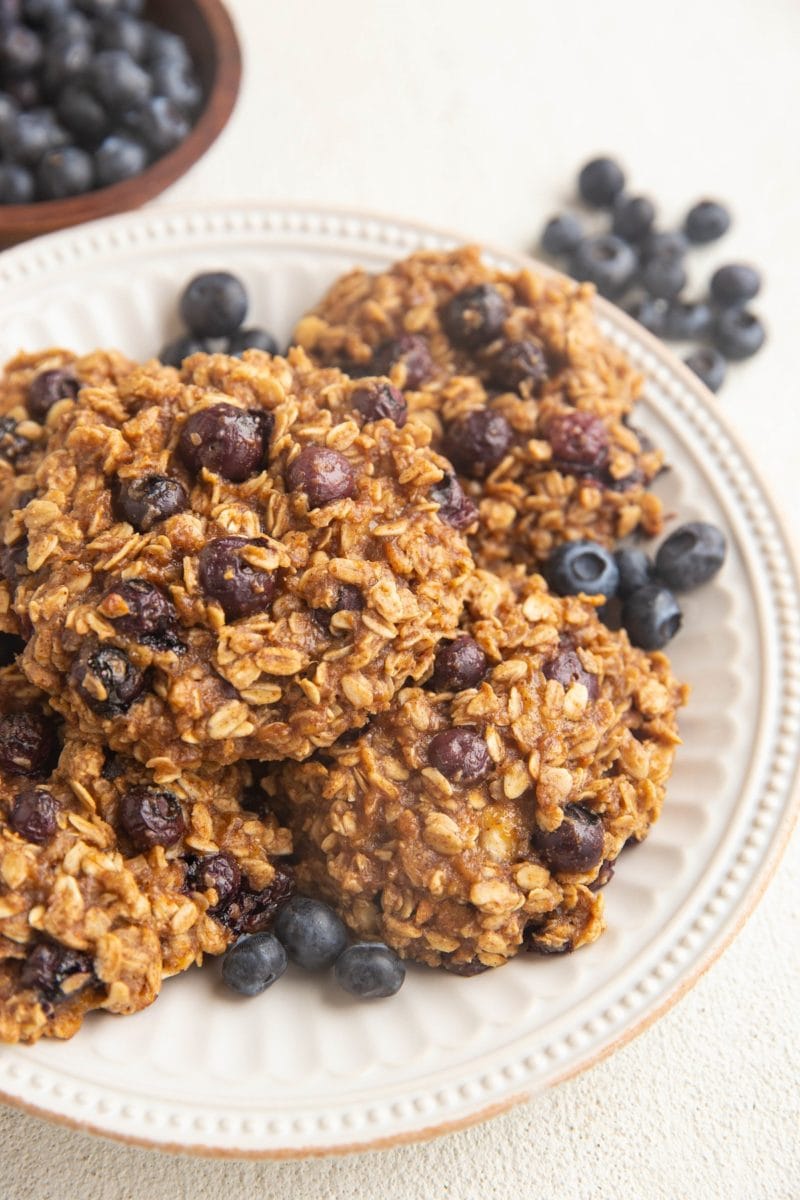 White plate of blueberry oatmeal breakfast cookies. Fresh blueberries all around.