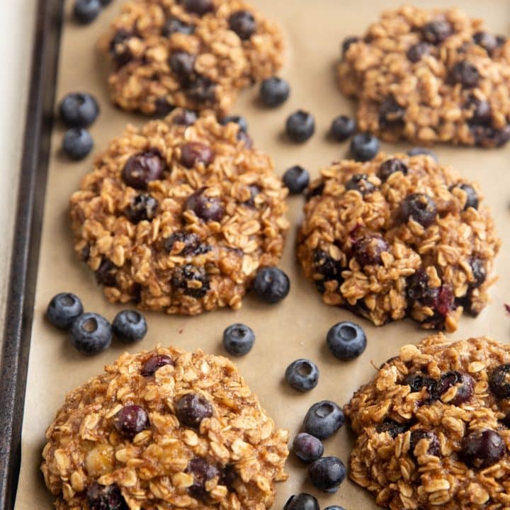 Blueberry Oatmeal Cookies on a baking sheet with fresh blueberries scattered around.