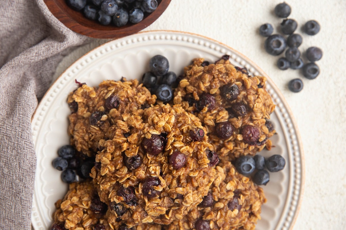 White plate of blueberry oatmeal cookies with fresh blueberries all around.