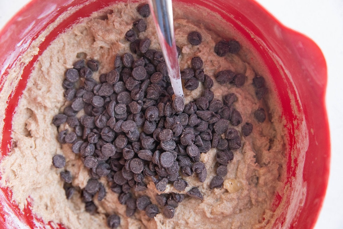 Banana bread batter in a red mixing bowl with chocolate chips on top.