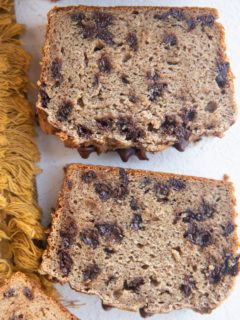 Slices of cassava flour banana bread on white background with a golden napkin to the side.