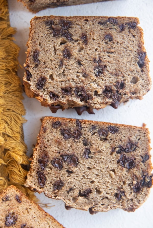 Slices of cassava flour banana bread on white background with a golden napkin to the side.