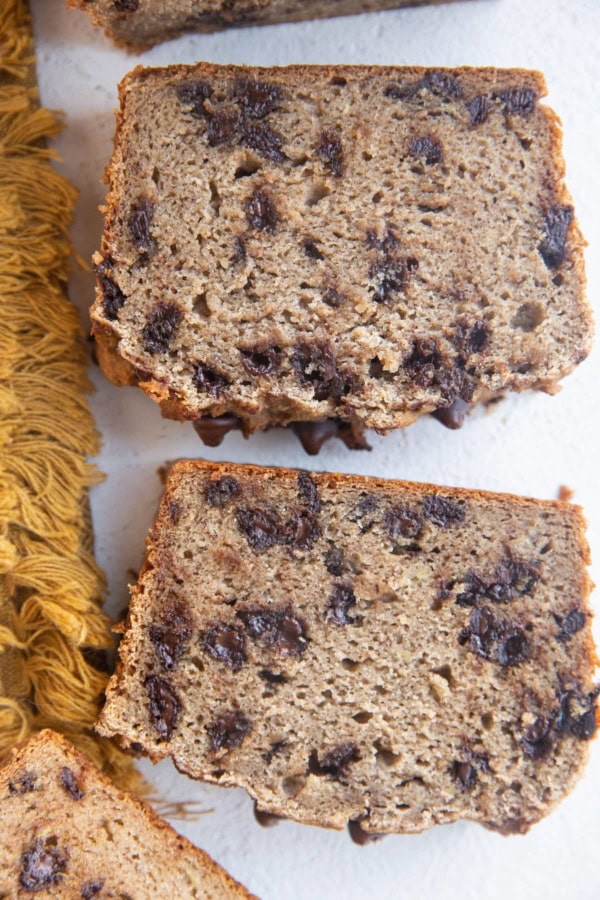 Slices of cassava flour banana bread on white background with a golden napkin to the side.
