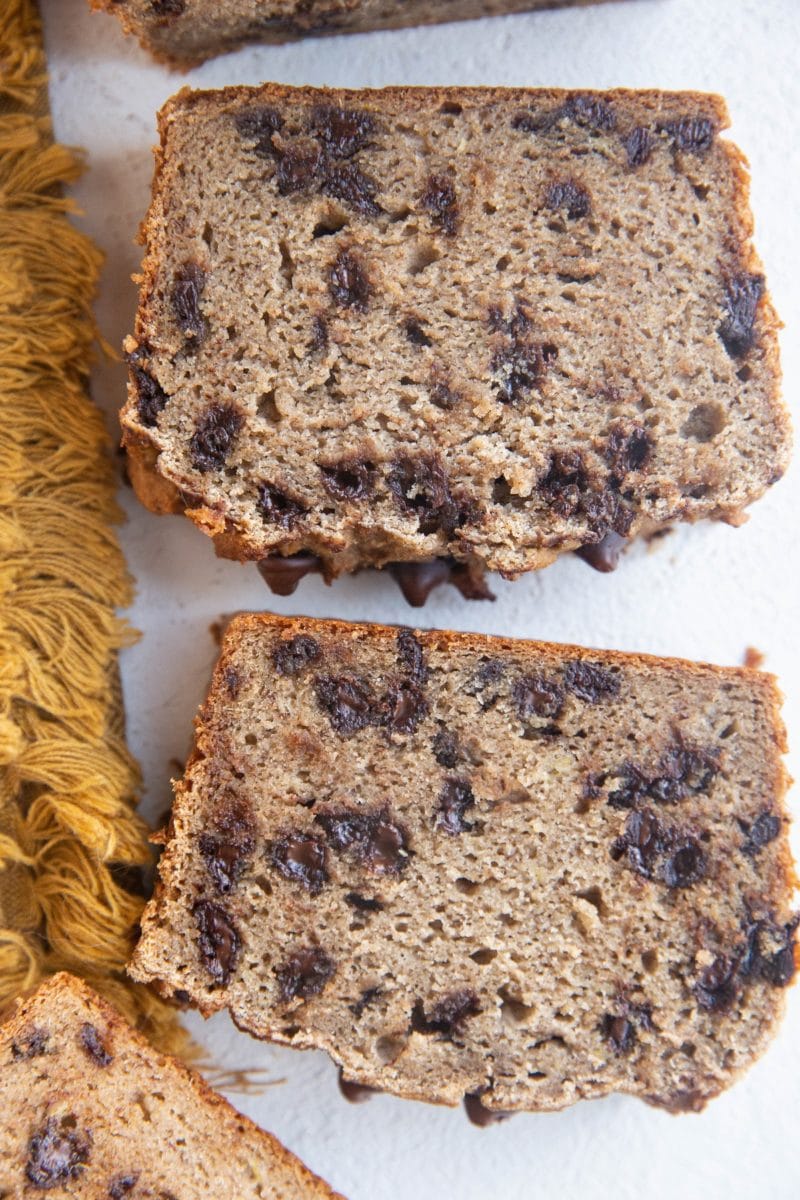 Slices of cassava flour banana bread on white background with a golden napkin to the side.