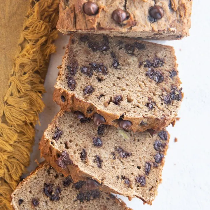 Loaf of grain-free banana bread cut into slices on a white backdrop with a gold napkin to the side.