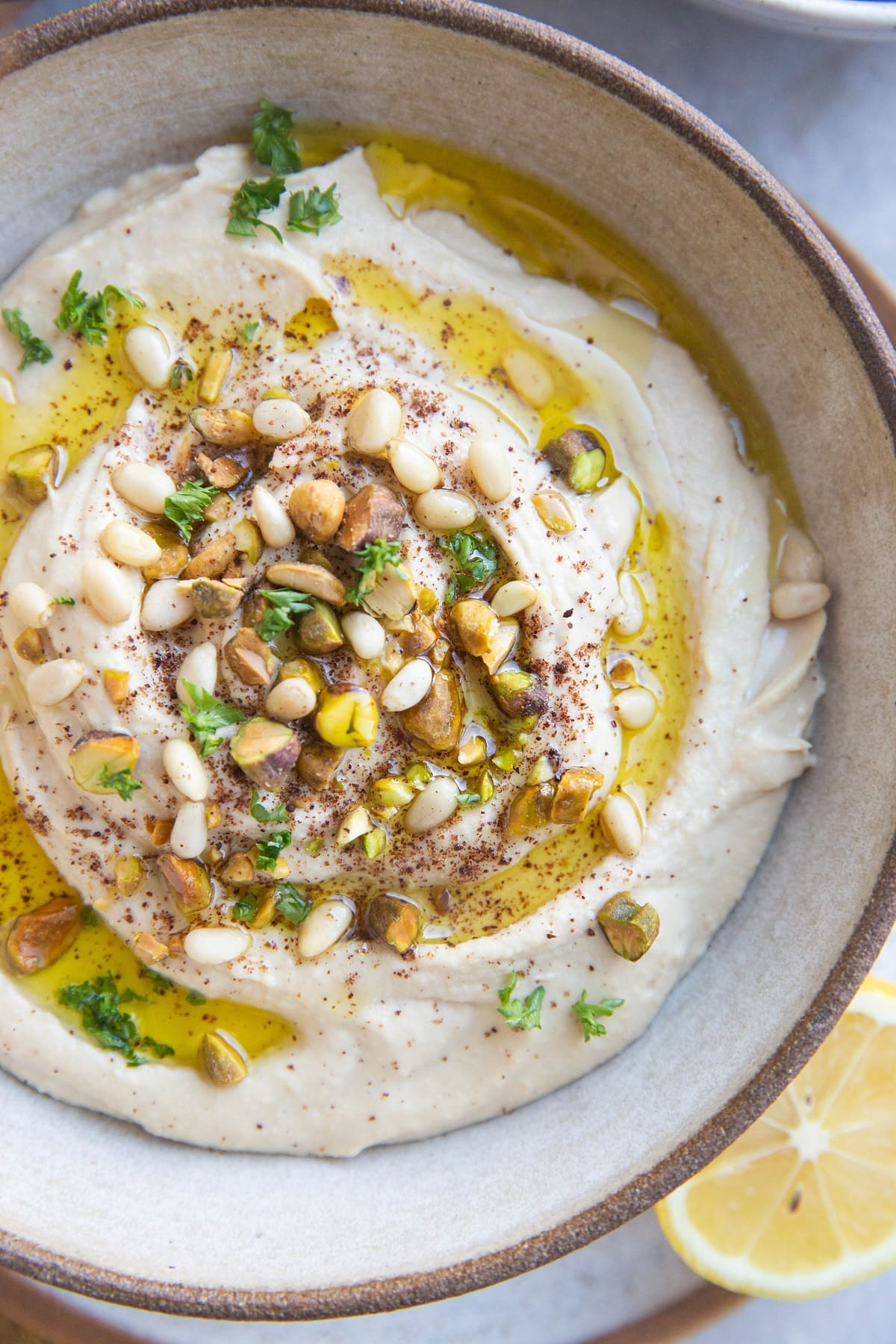 Big bowl of hummus with fresh parsley sprinkled on top and pine nuts and pistachios. Ready to serve.