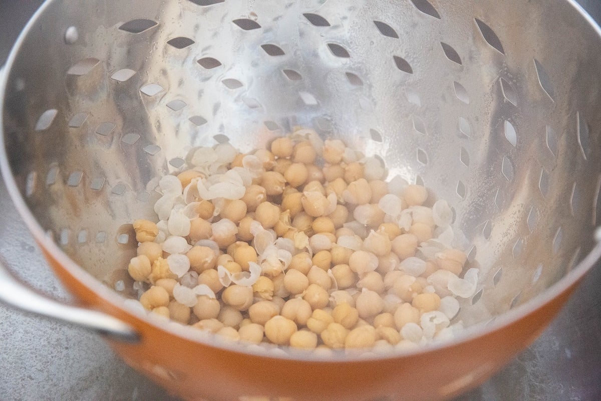 Boiled chickpeas in a colander with skins off, ready to be removed.