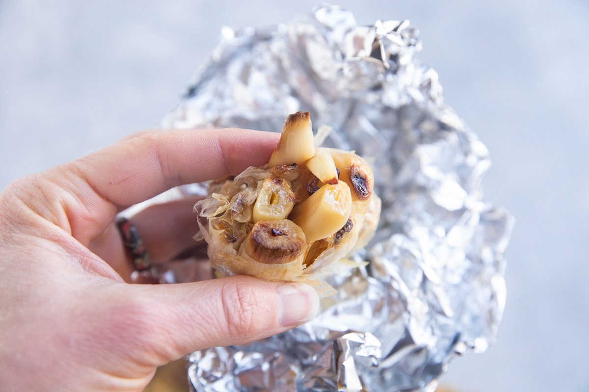 Hand holding a bulb of roasted garlic, pressing the cloves out of the bulb.