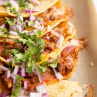 Pile of ground beef and cheese tacos laying on top of each other with cilantro and red onion sprinkled on top.