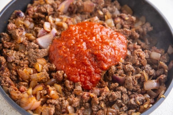 Ground beef taco meat in a skillet with tomato sauce being mixed in.