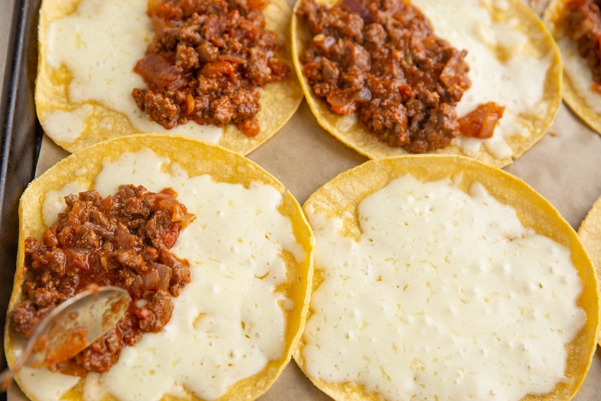 Spoon spreading beef taco mixture on top of the melted cheese tortillas.