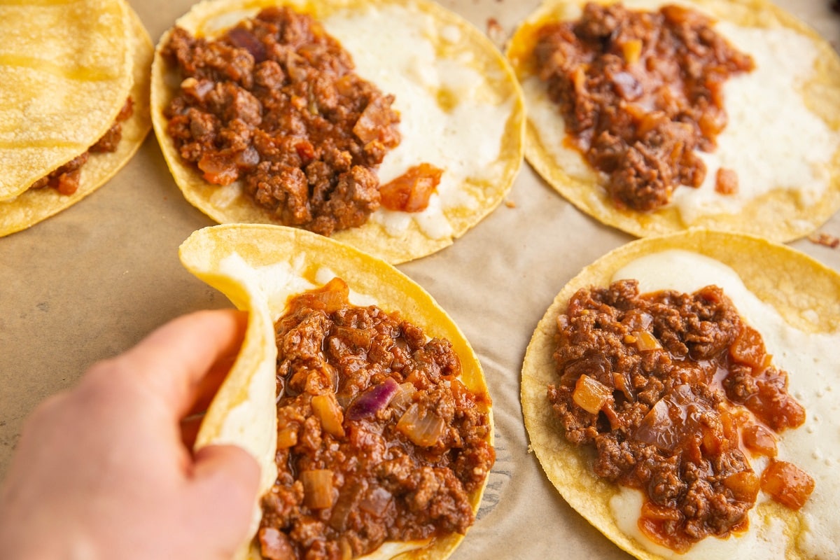 Hand folding over the taco shell to form tacos.