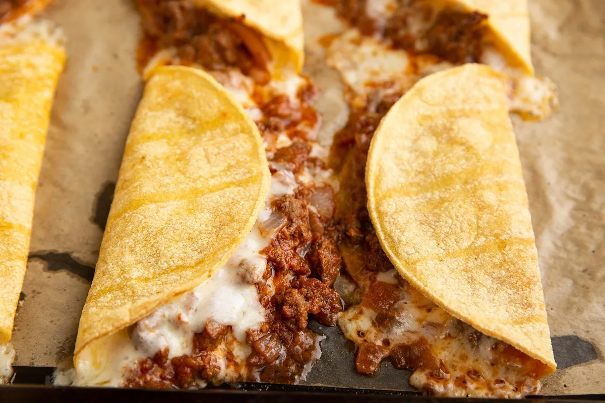Crispy baked ground beef tacos fresh out of the oven with meat and cheese melting out.
