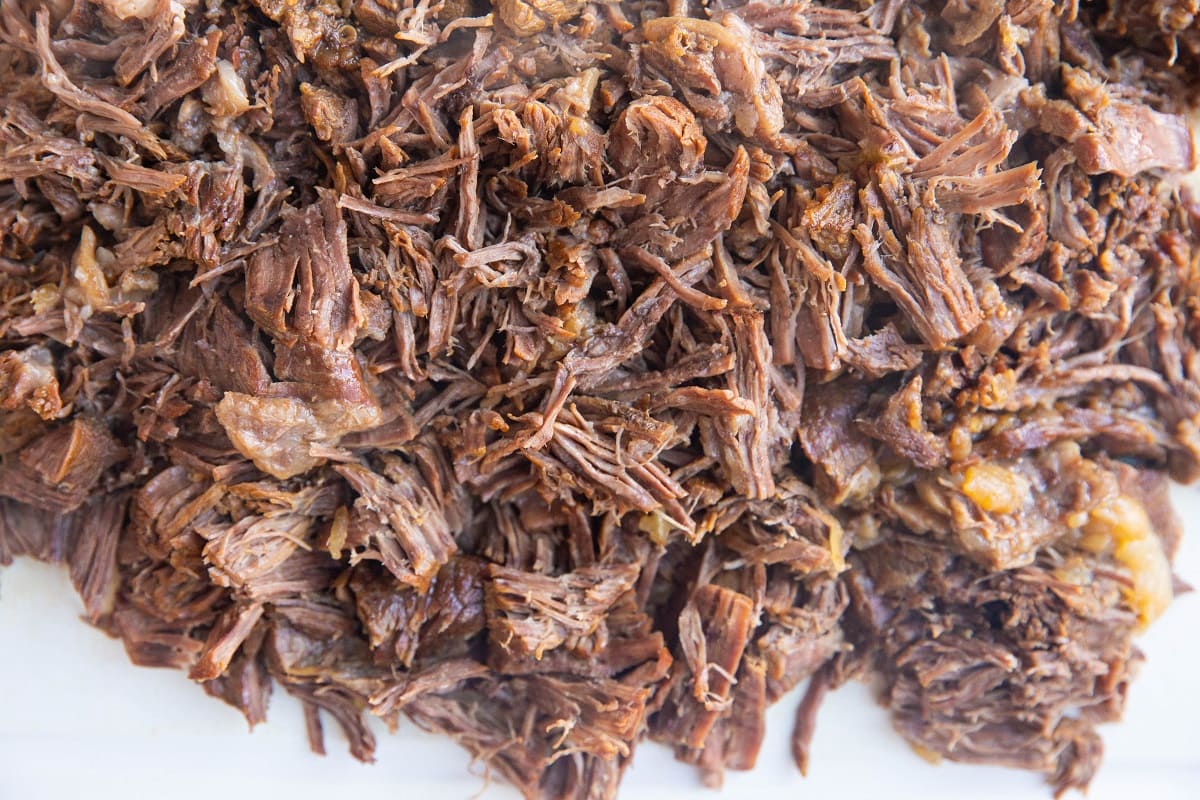 Cutting board with shredded beef on top.