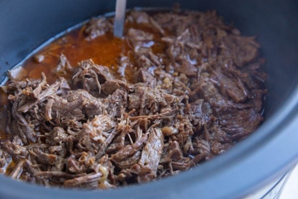 Horizontal image of a crock pot full of shredded beef.