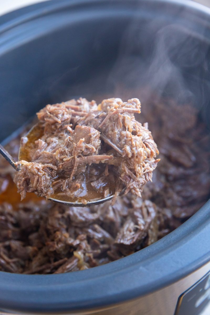 Ladle scooping shredded beef out of a slow cooker.
