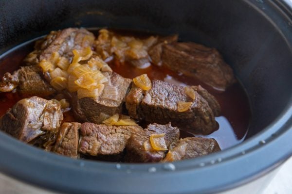 Cooked beef in a slow cooker with juices inside.