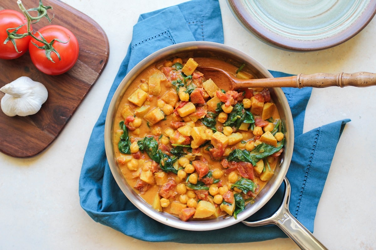 Stainless steel skillet with finished chickpea and spinach curry, ready to serve.