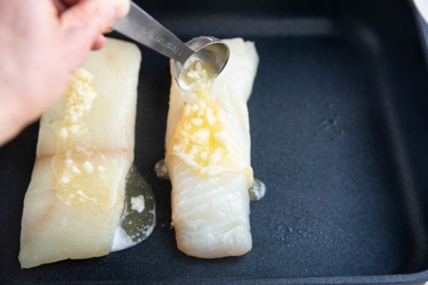 Hand pouring a tablespoon of garlic butter mixture over raw halibut filets