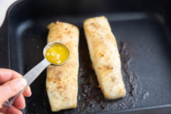 Hand holding a tablespoon of butter, ready to pour on cooked halibut.