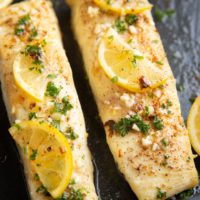 Two cooked halibut filets with butter, fresh garlic, and lemon on top