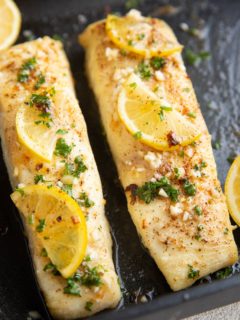 Two cooked halibut filets with butter, fresh garlic, and lemon on top