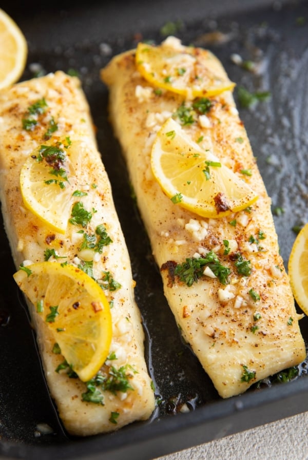 Two cooked halibut filets with butter, fresh garlic, and lemon on top