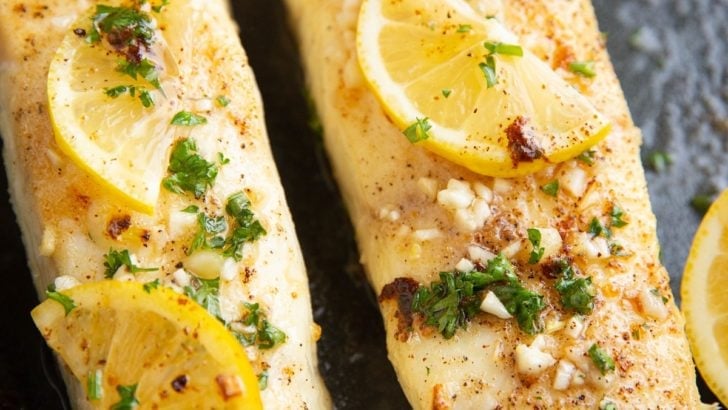 Two cooked halibut filets with butter, fresh garlic, and lemon on top