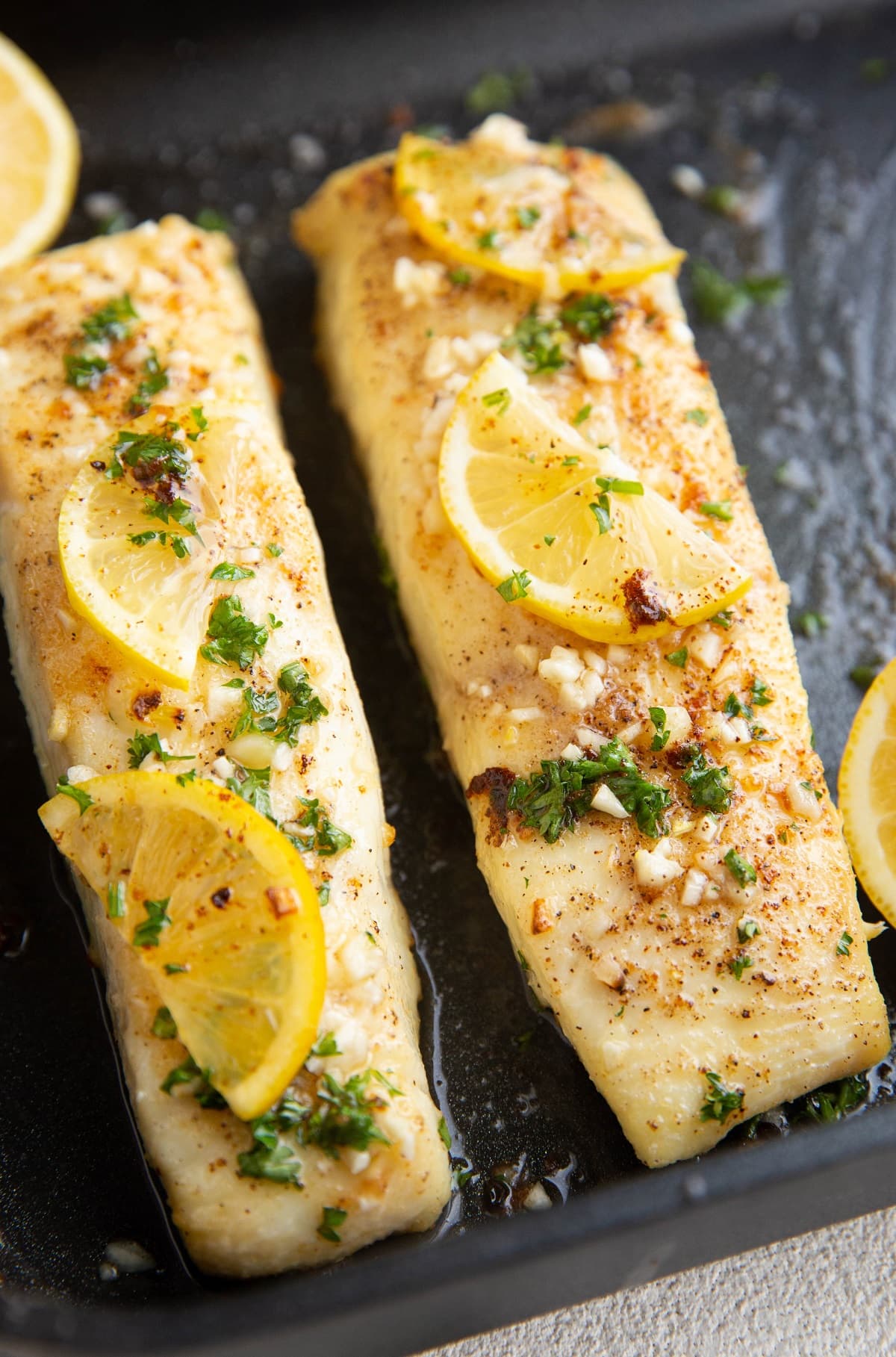 Two cooked halibut filets with butter, fresh garlic, and lemon on top