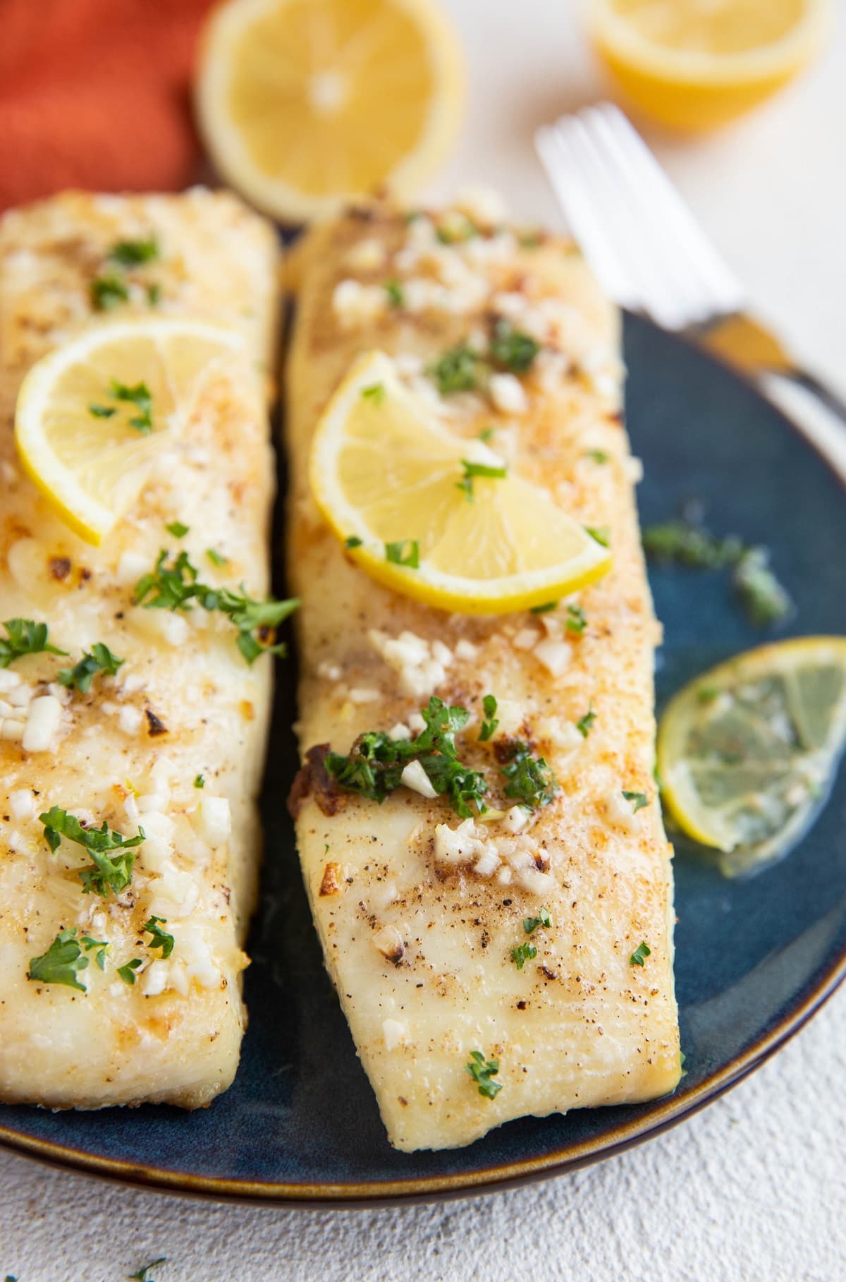 Blue plate with two freshly baked halibut filets on top, ready to be served with side dishes.