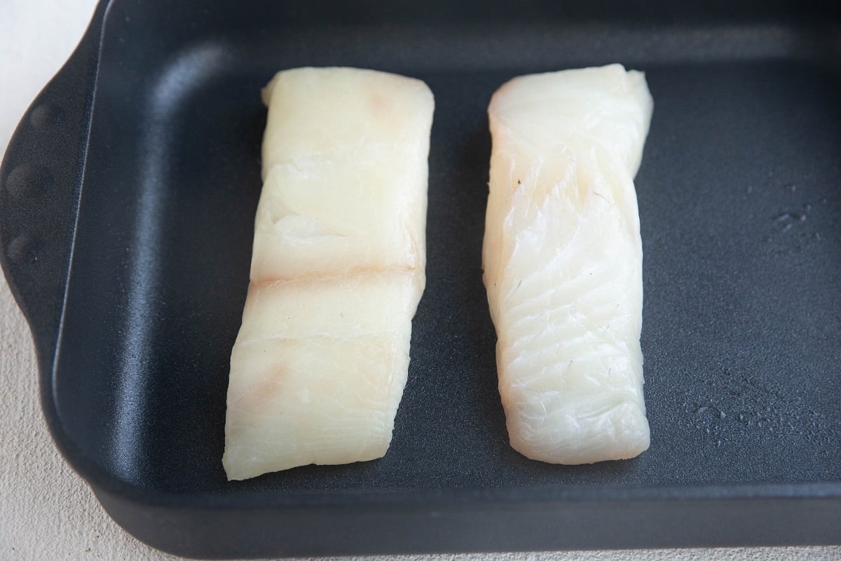 Two large raw halibut filets in a large casserole dish.