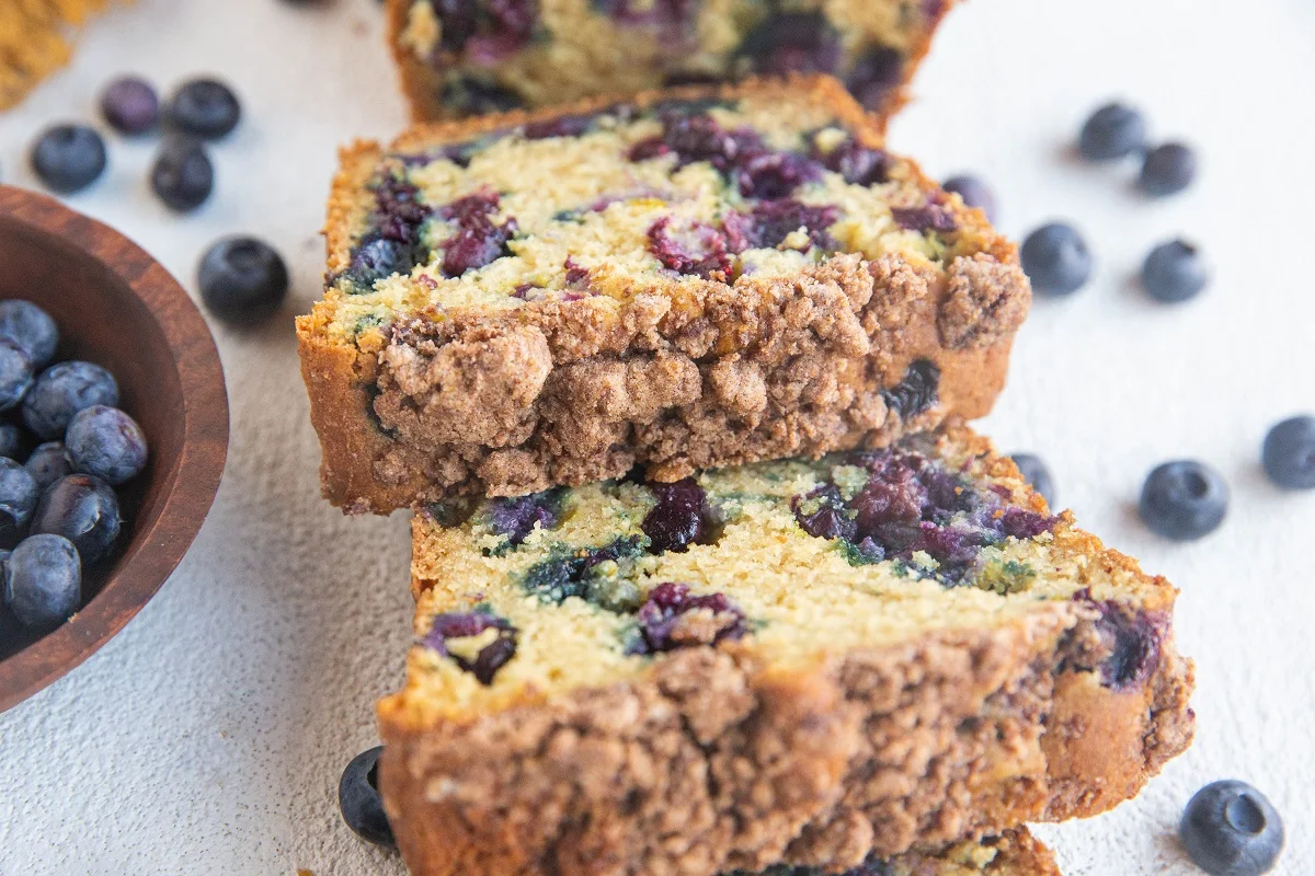 Slices of blueberry bread on top of each other with fresh blueberries all around.