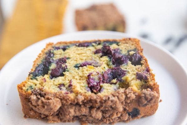 White plate with a slice of blueberry bread on top.