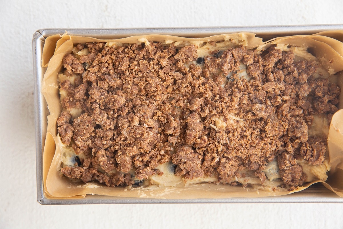 Crumb topping mixture sprinkled over the blueberry muffin batter, ready to go into the oven to bake.