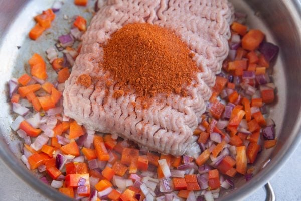 Ground turkey and chili powder on top of onion and bell pepper for taco meat.