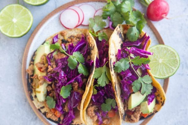 Plate with three ground turkey tacos with fresh cilantro and red cabbage slaw on top.