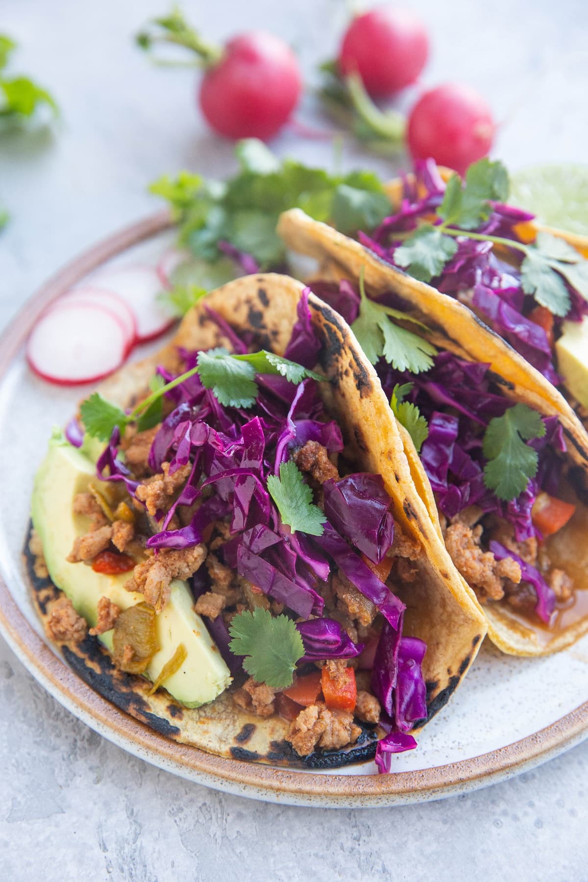 Three tacos on a plate with corn tortillas, avocado and cabbage slaw.