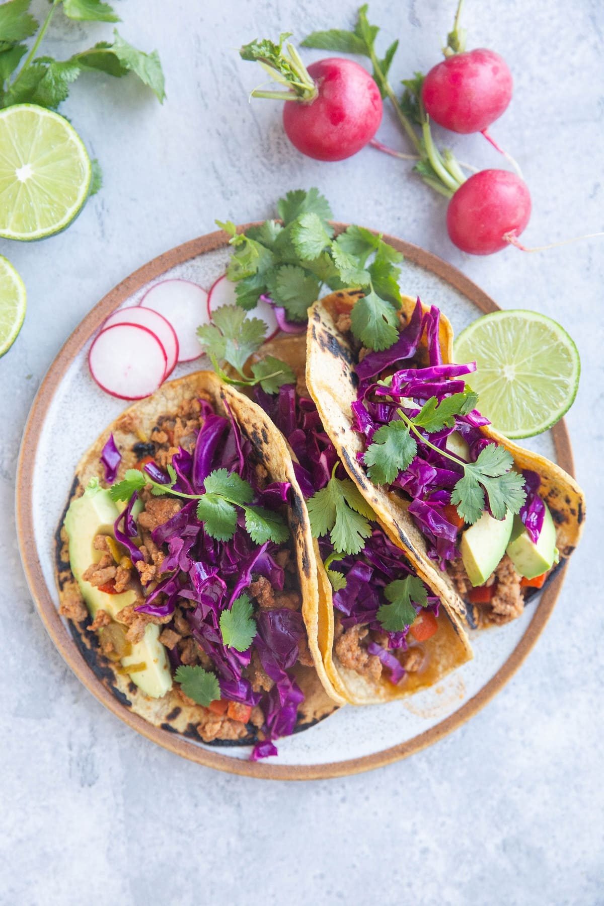 Plate of three tacos with ground turkey, slaw, avocado and fresh cilantro.