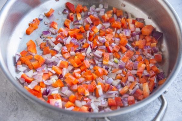 Bell pepper and onion sautéing in a stainless steel skillet.