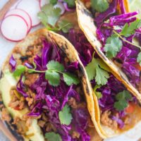 Close up of three tacos with slaw and fresh herbs on top.