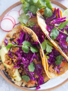 Close up of three tacos with slaw and fresh herbs on top.