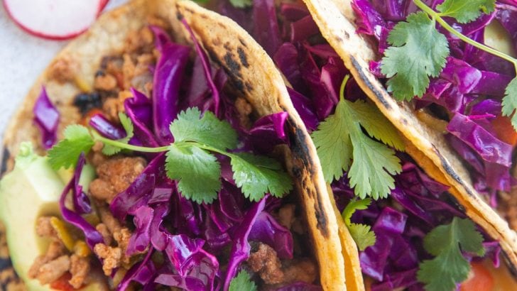 Close up of three tacos with slaw and fresh herbs on top.