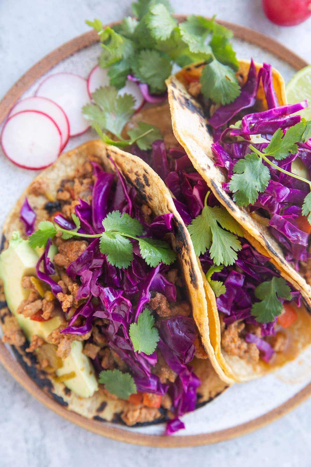 Close up of three tacos with slaw and fresh herbs on top.
