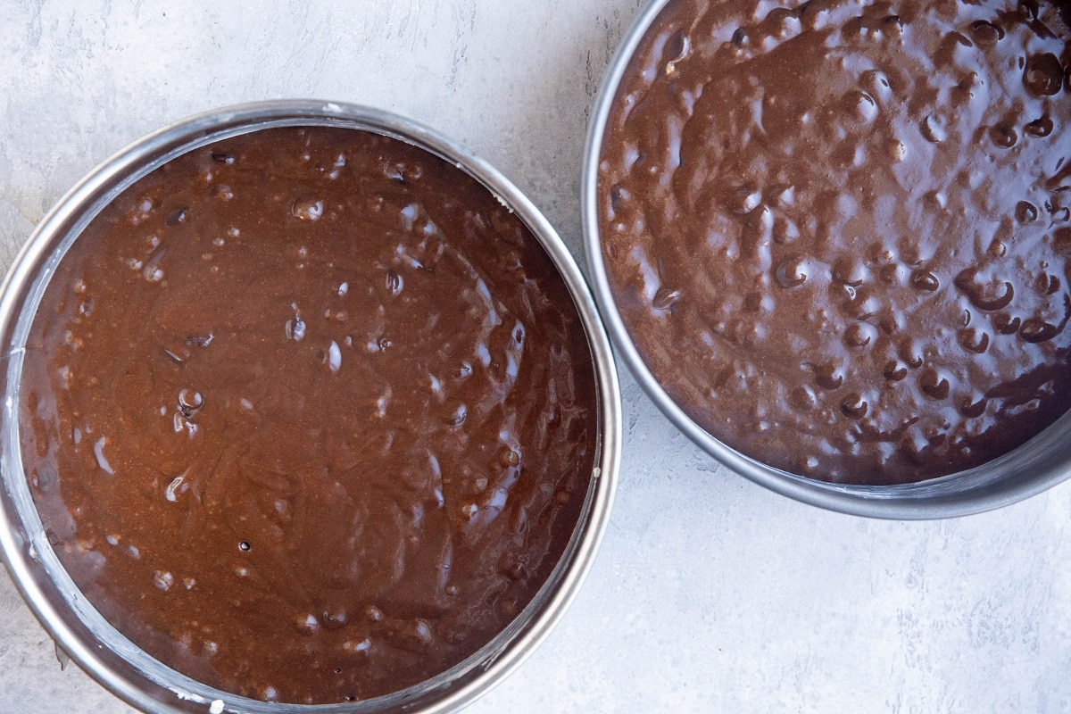 Two springform pans with chocolate cake batter inside, ready to bake.