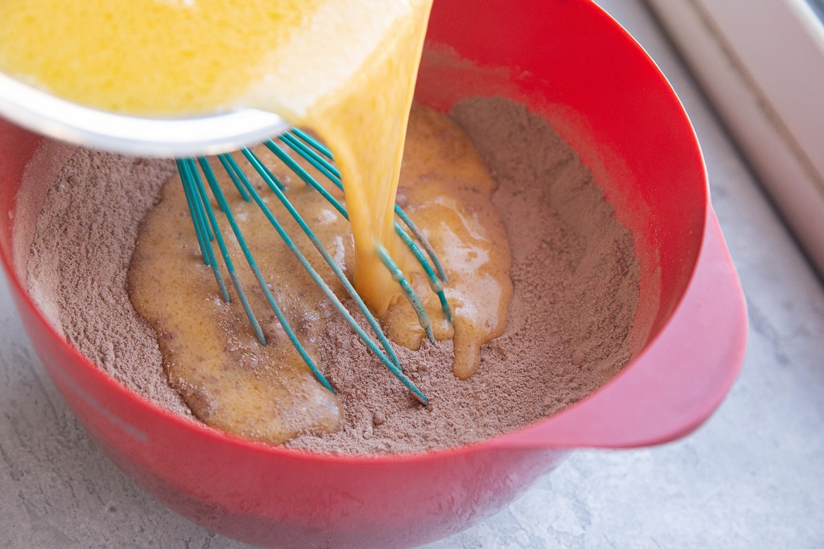 Pouring wet ingredients into a large bowl with the dry ingredients.