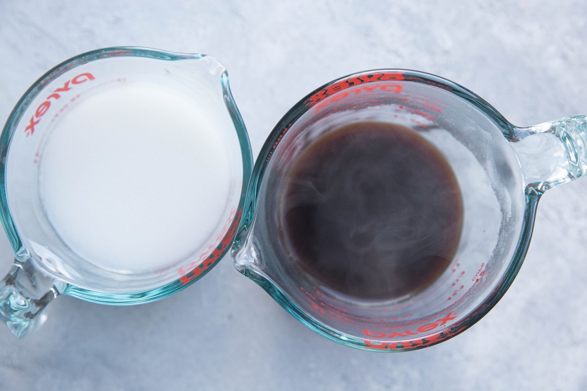 Hot coffee in a measuring cup and coconut milk in another measuring cup.